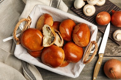 Photo of Wicker basket with delicious baked mushrooms and onion pirozhki on wooden table, flat lay