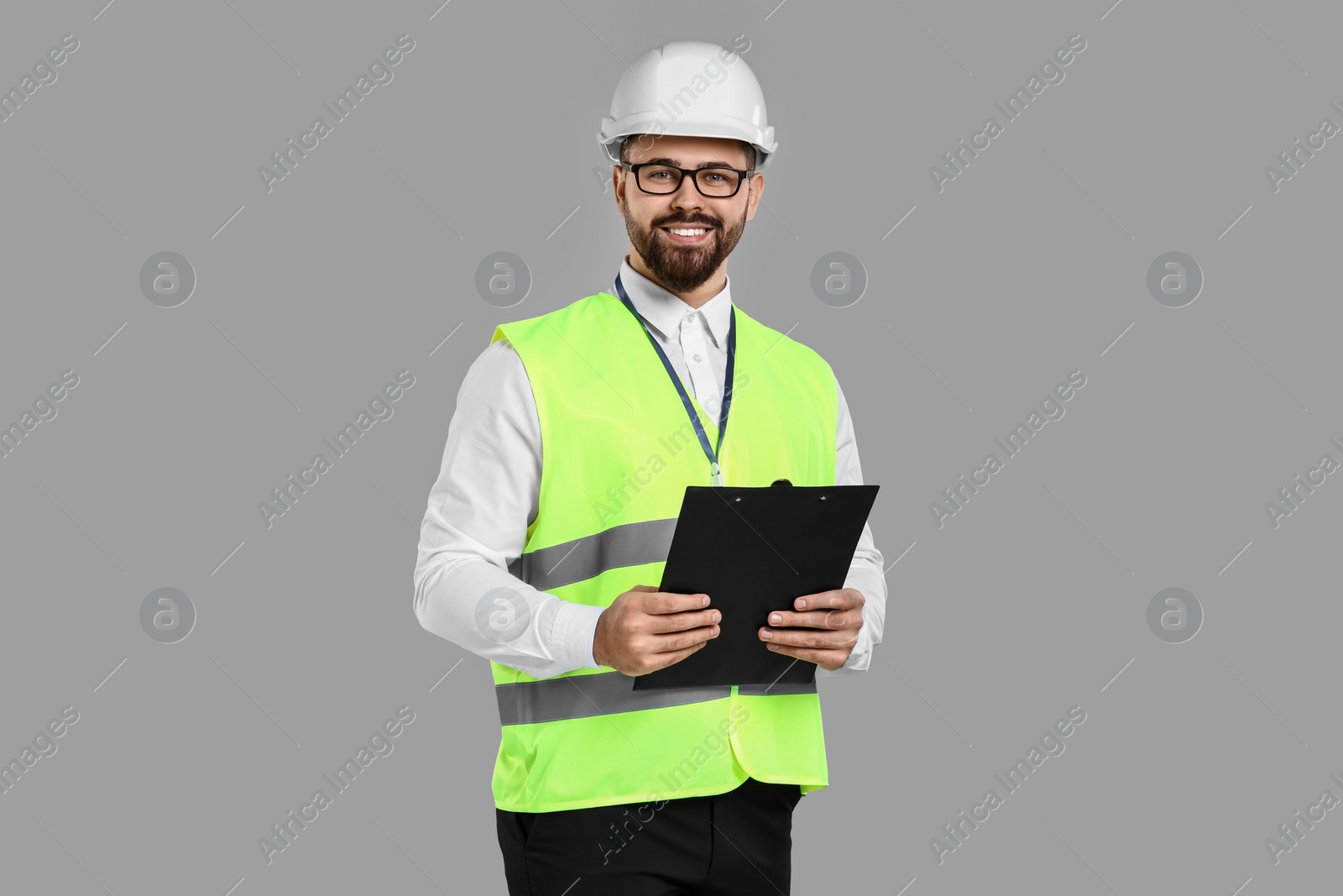 Photo of Engineer in hard hat holding clipboard on grey background