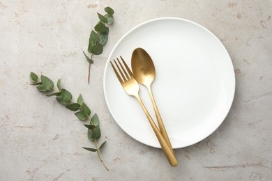 Stylish setting with cutlery, eucalyptus branches and plate on light grey table, flat lay