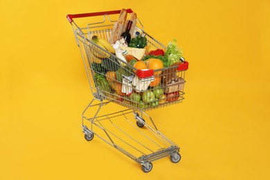 Photo of Shopping cart full of groceries on yellow background