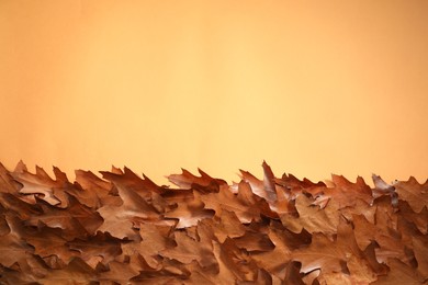 Photo of Dry autumn leaves on pale orange background, top view. Space for text