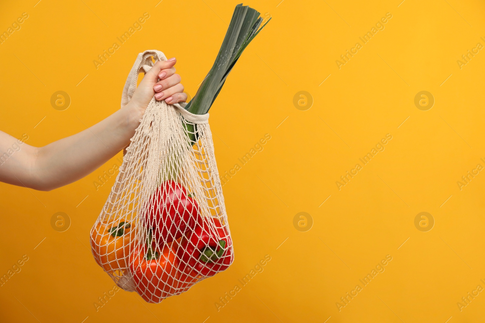 Photo of Woman with string bag of fresh vegetables on orange background, closeup. Space for text