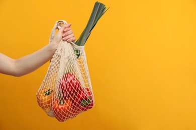 Photo of Woman with string bag of fresh vegetables on orange background, closeup. Space for text