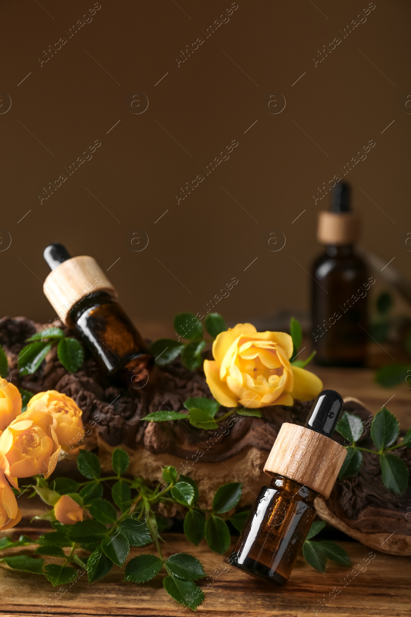 Photo of Bottles of rose essential oil and flowers on wooden table