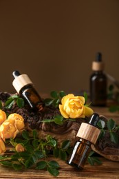 Photo of Bottles of rose essential oil and flowers on wooden table