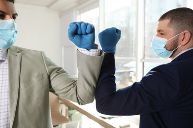 Photo of Office employees in masks greeting each other by bumping elbows at workplace