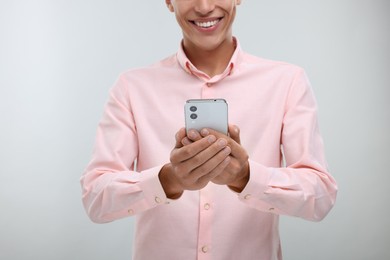 Young man sending message via smartphone on light grey background, closeup