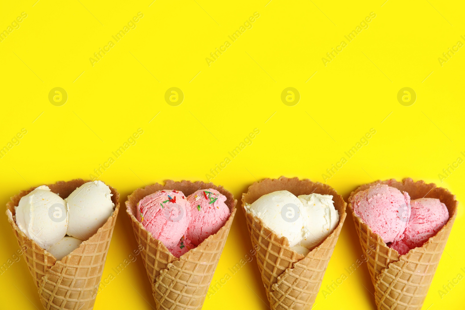 Photo of Delicious ice creams in wafer cones on yellow background, flat lay. Space for text