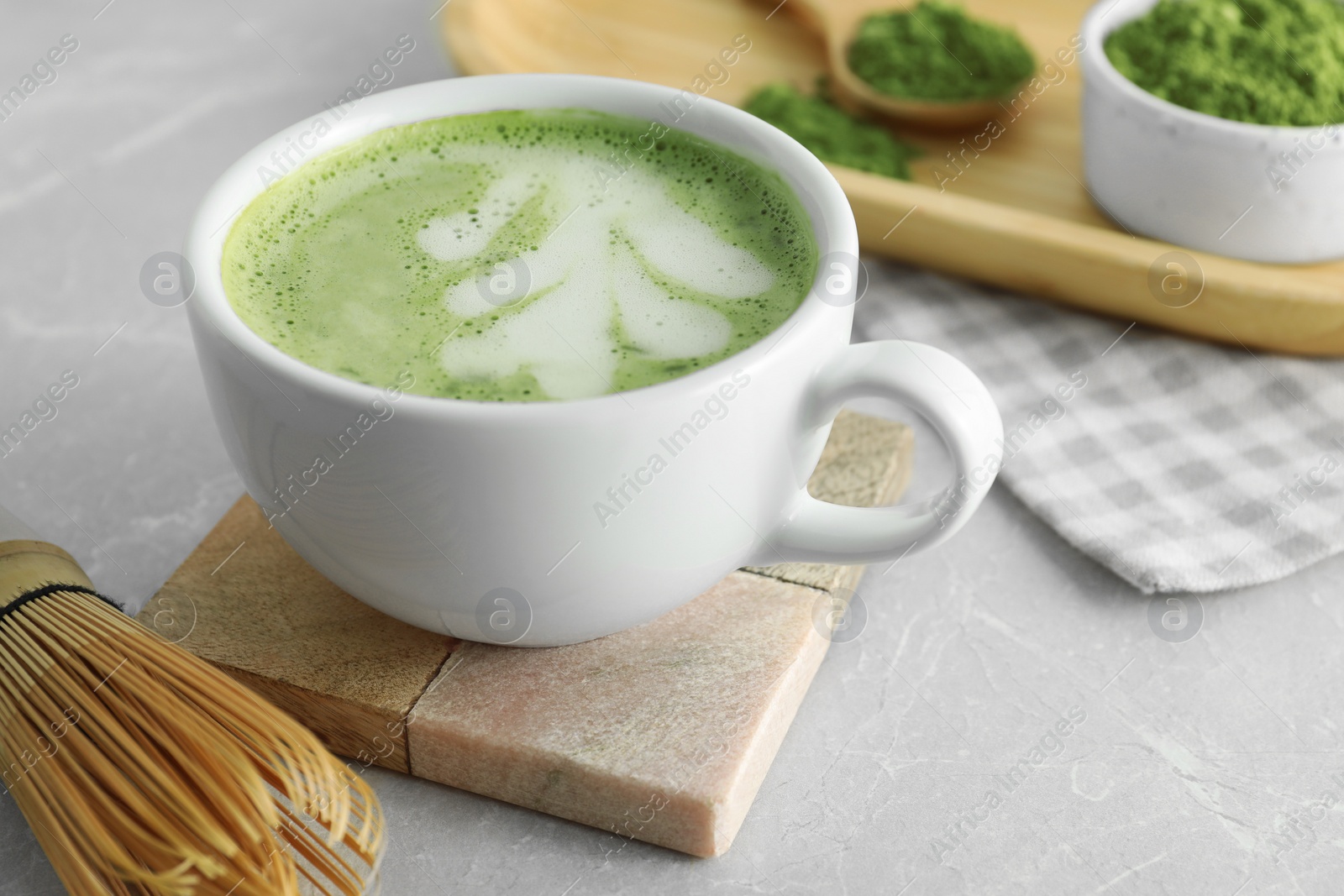 Photo of Cup of fresh matcha latte and bamboo whisk on light grey table, closeup