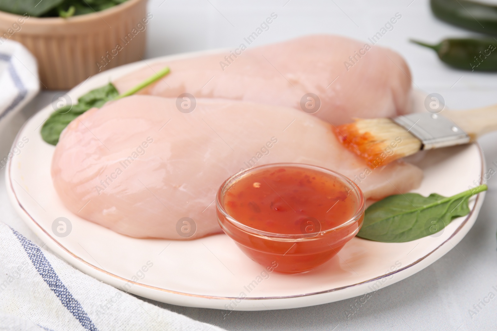 Photo of Marinade, basting brush and raw chicken fillets on white table, closeup