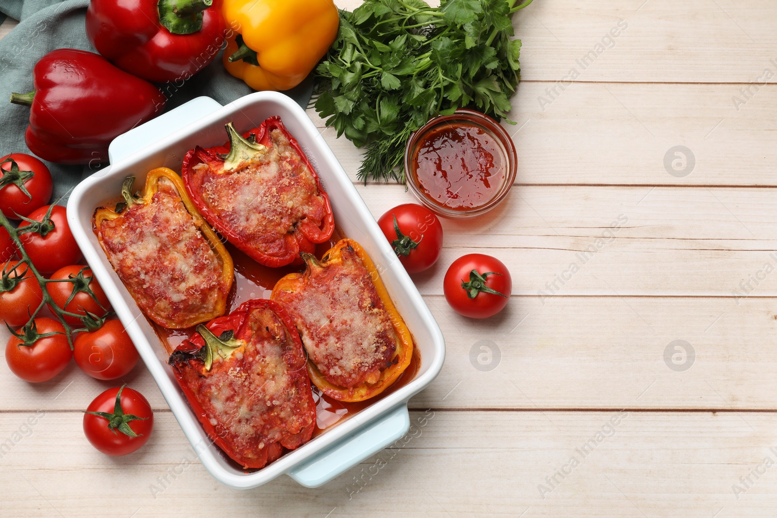 Photo of Tasty stuffed peppers in dish and ingredients on light wooden table, flat lay. Space for text