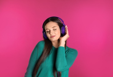 Attractive young woman enjoying music in headphones on color background