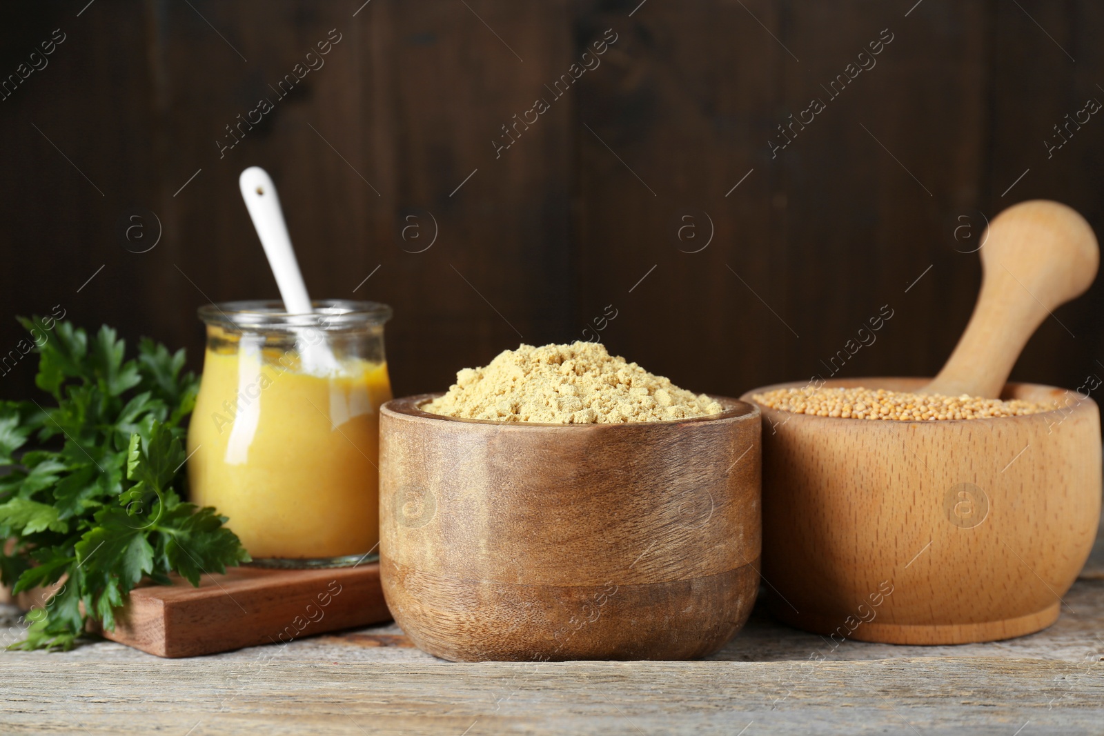 Photo of Bowl of mustard powder, parsley and mortar with seeds on wooden table