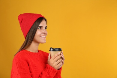 Happy beautiful woman with paper cup of mulled wine on yellow background. Space for text