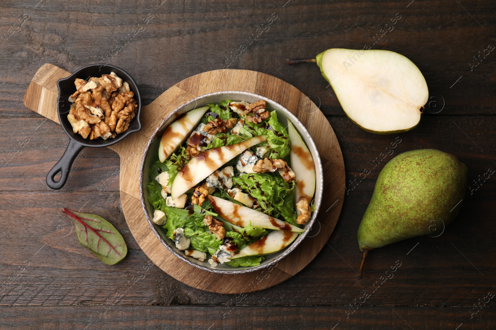 Photo of Delicious pear salad with sauce in bowl and ingredients on wooden table, flat lay