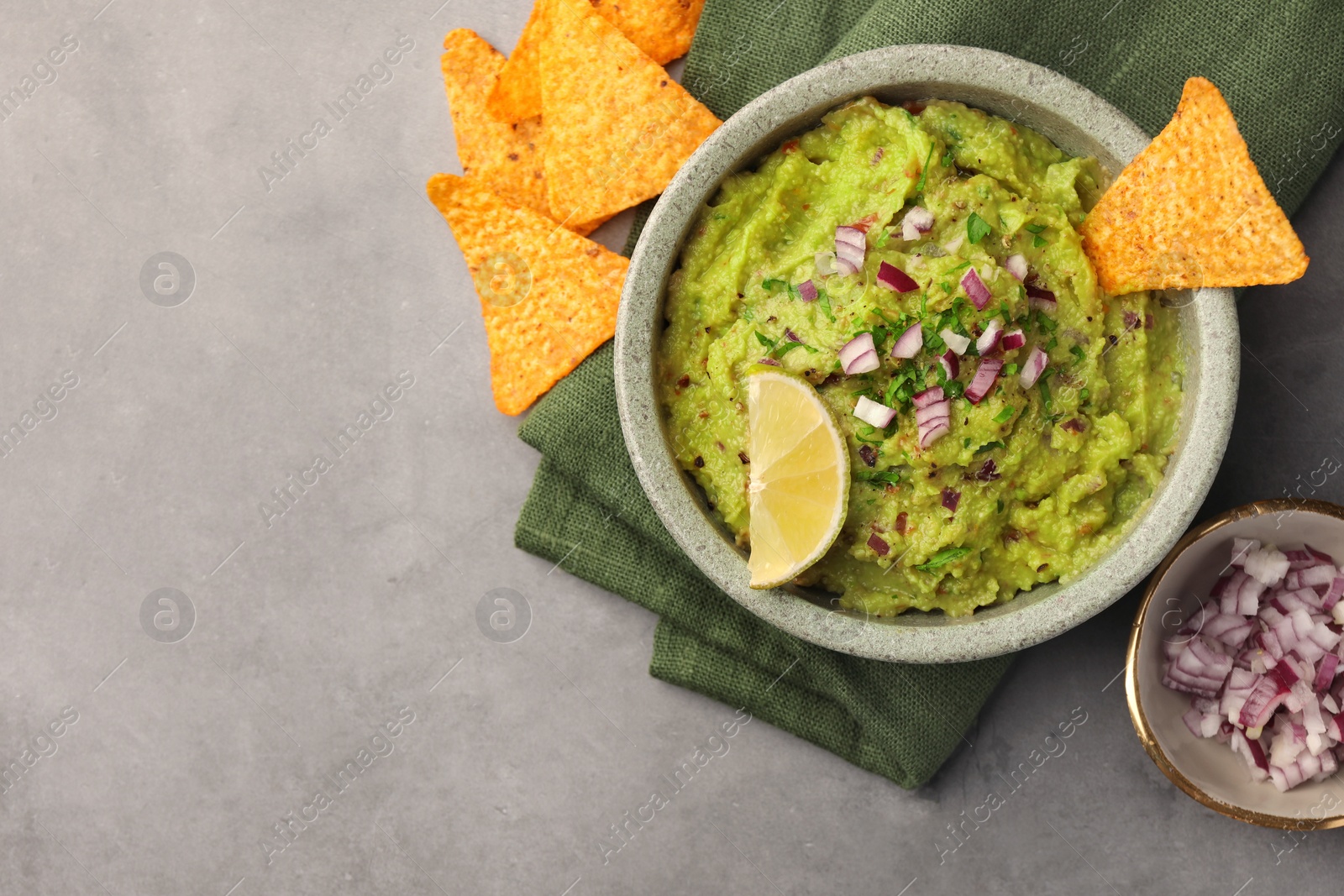 Photo of Bowl of delicious guacamole, nachos chips and lime on grey table, flat lay. Space for text