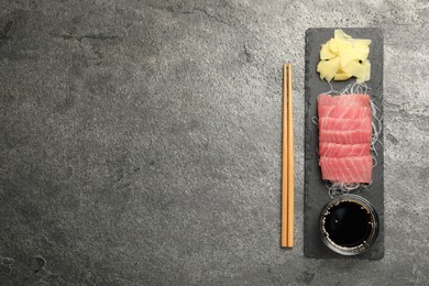 Photo of Tasty sashimi (pieces of fresh raw tuna, funchosa) served with soy sauce and ginger slices on gray table, flat lay. Space for text