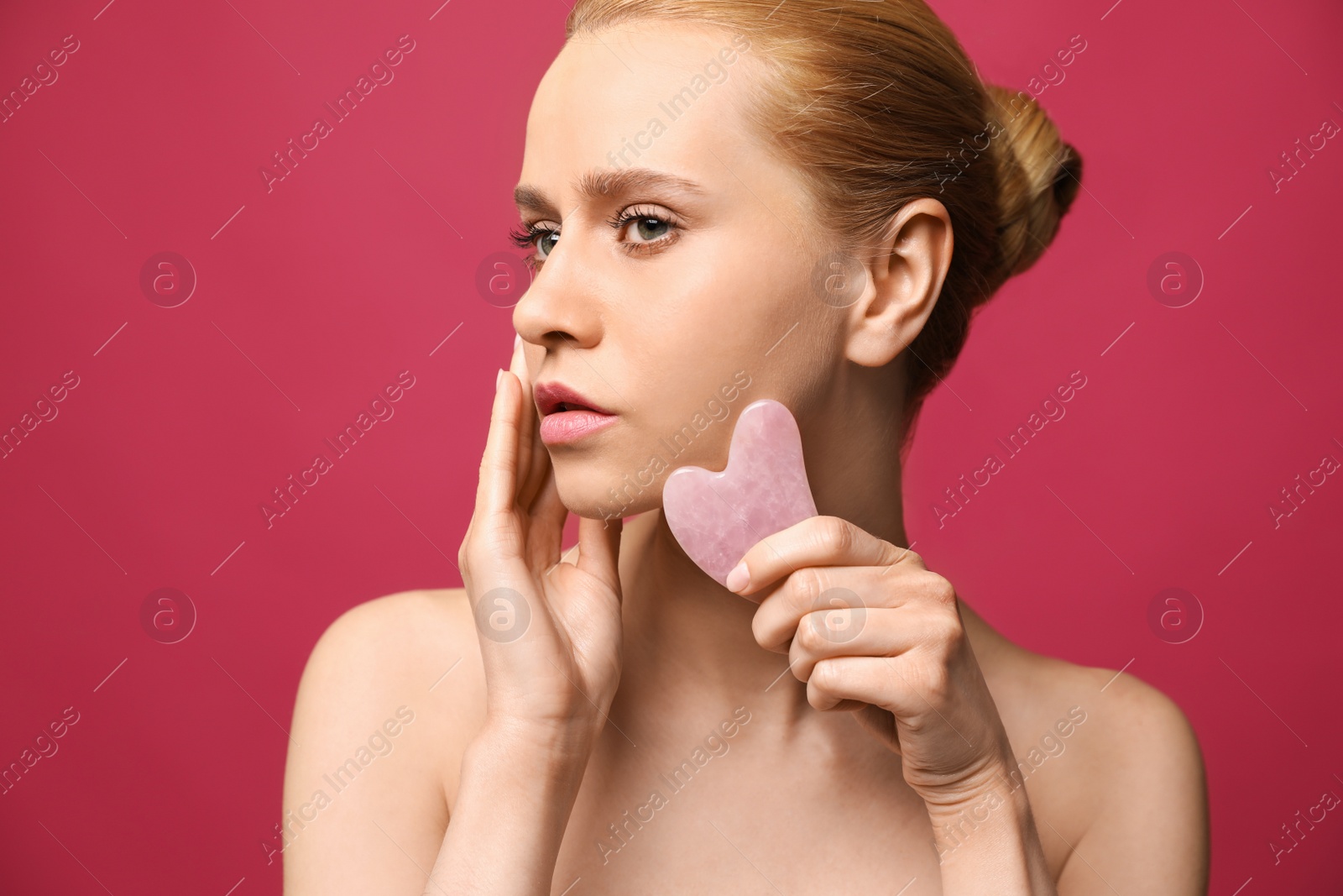 Photo of Beautiful young woman doing facial massage with gua sha tool on pink background