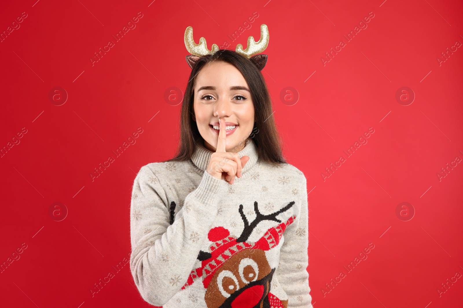 Photo of Young woman in Christmas sweater and deer headband on red background