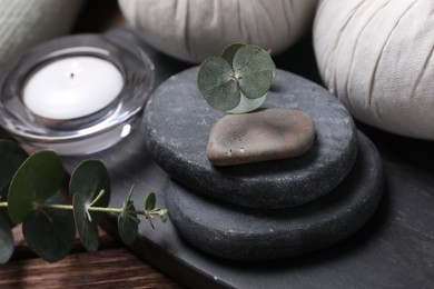 Photo of Beautiful spa composition with herbal massage bags, stones and eucalyptus branches on wooden table, closeup