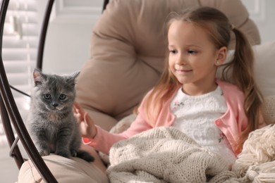 Photo of Cute little girl with kitten in hanging chair at home. Childhood pet