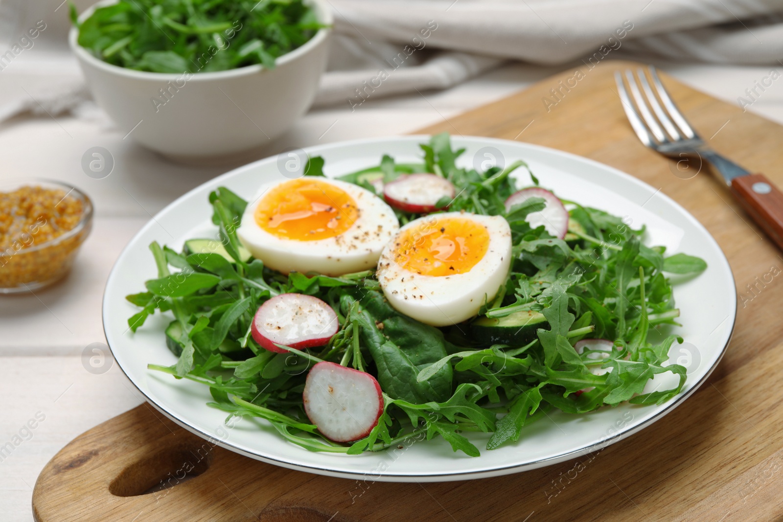 Photo of Delicious salad with boiled egg, vegetables and arugula on wooden board, closeup