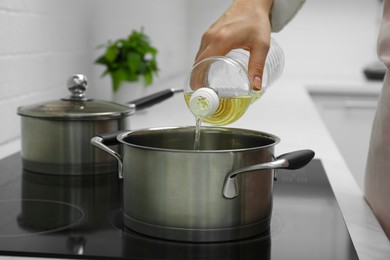 Woman pouring cooking oil from bottle into pot in kitchen, closeup