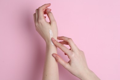 Woman applying cream on her hand against pink background, closeup