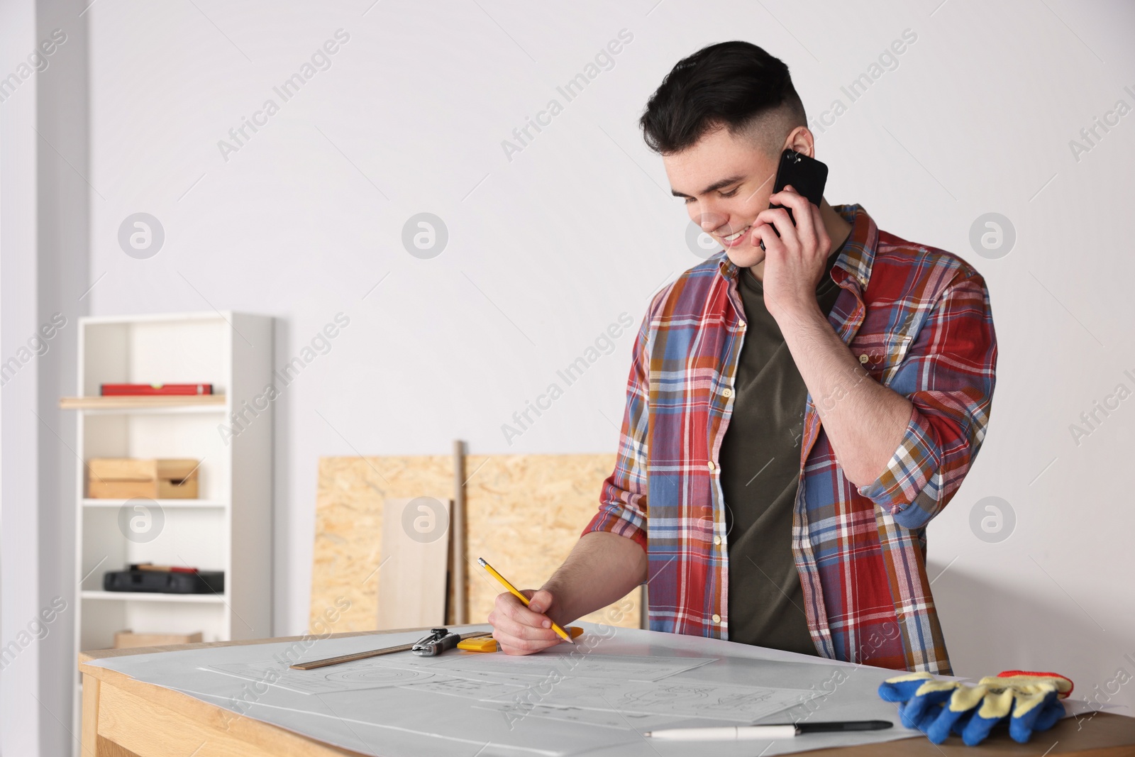 Photo of Handyman working with blueprints and talking on phone in room