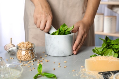 Photo of Woman making basil pesto sauce at kitchen table