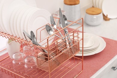 Drying rack with clean dishes and cutlery on countertop in kitchen