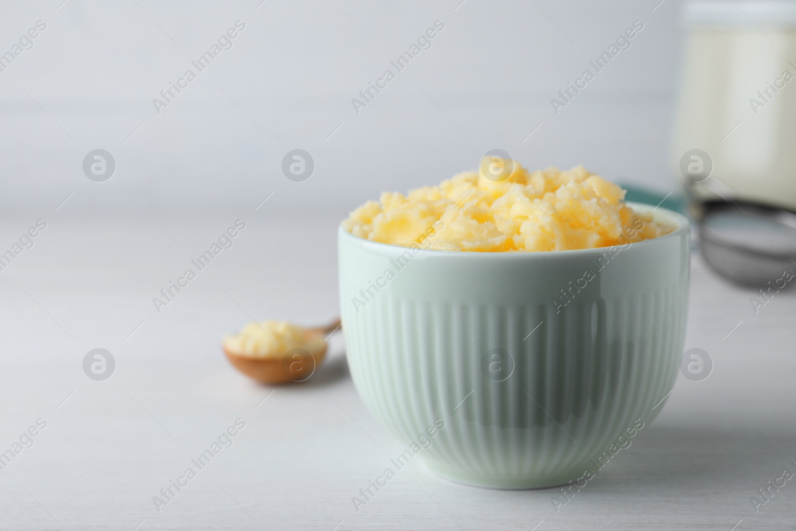 Photo of Bowl of Ghee butter on white wooden table. Space for text