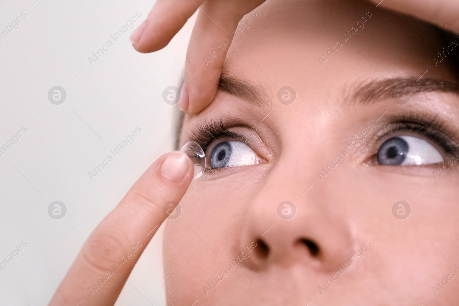 Photo of Young woman putting contact lens in her eye on light background, closeup