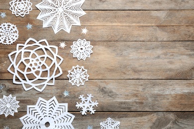 Flat lay composition with paper snowflakes on wooden background, space for text. Winter season