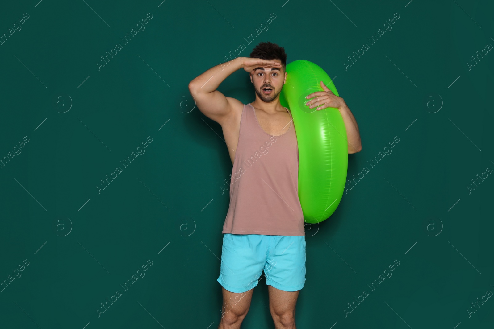 Photo of Funny young man with bright inflatable ring on dark green background, space for text