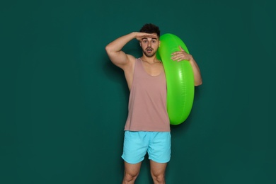 Funny young man with bright inflatable ring on dark green background, space for text