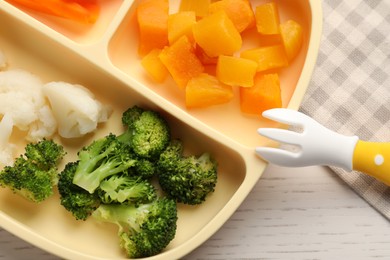 Photo of Baby food. Section plate with different vegetables on white wooden table, top view