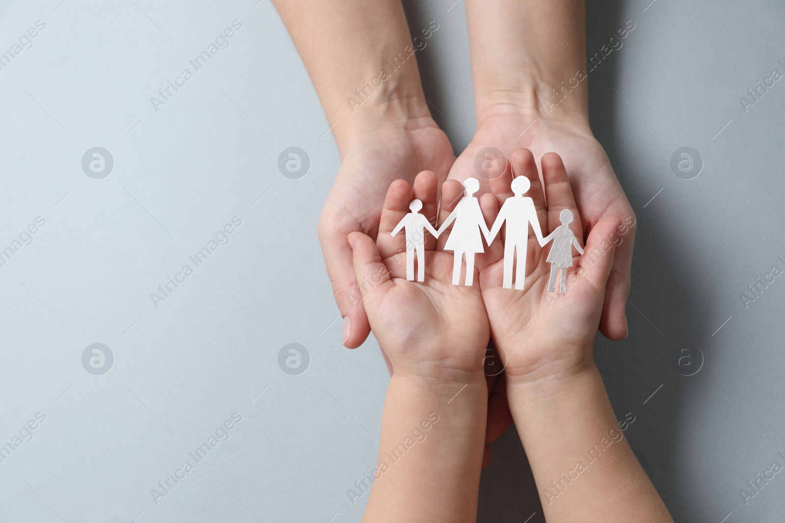 Photo of Parents and child holding paper family figures on gray background, top view. Space for text