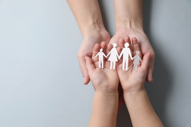 Parents and child holding paper family figures on gray background, top view. Space for text