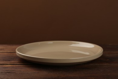 Beautiful ceramic plate on wooden table against brown background, space for text