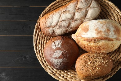 Photo of Wicker basket with different types of fresh bread on black wooden table, top view
