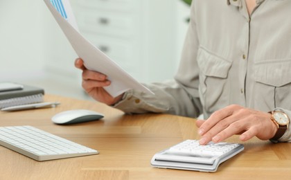 Professional accountant using calculator at wooden desk in office, closeup