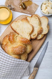 Photo of Cut freshly baked braided bread, honey and butter on white wooden table, flat lay. Traditional Shabbat challah
