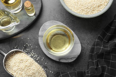 Photo of Sesame oil and seeds on dark grey table, flat lay