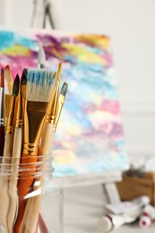 Different paintbrushes in glass on blurred background, closeup. Space for text