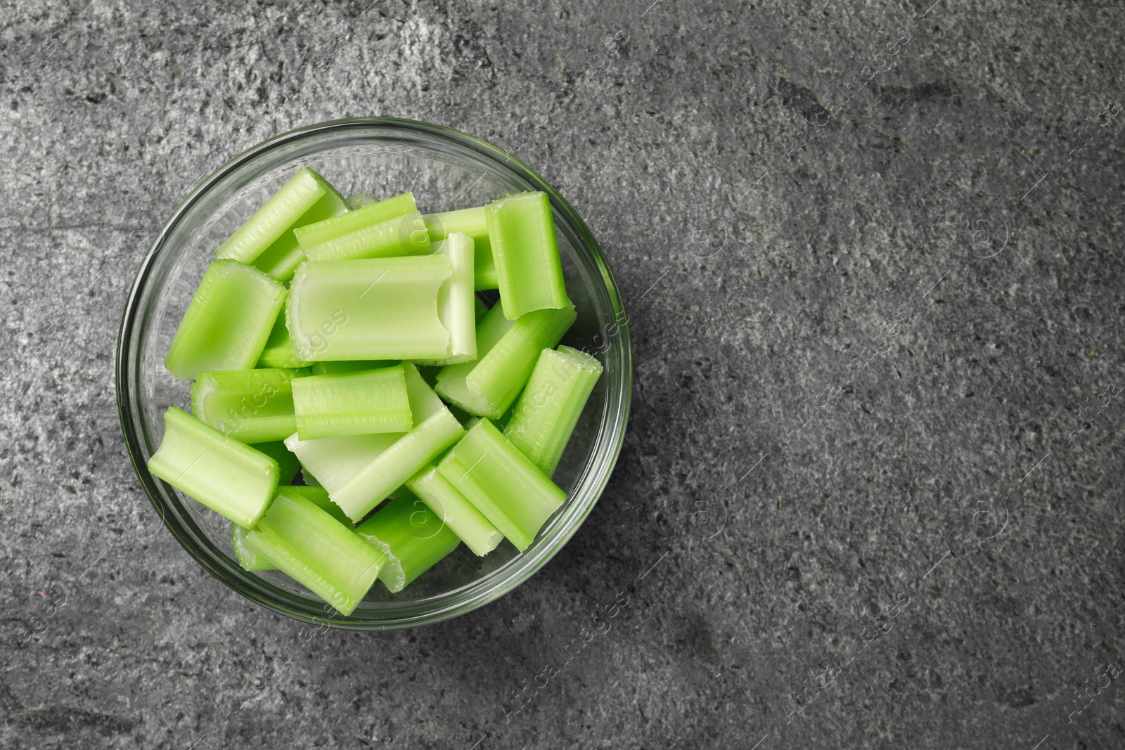 Photo of Bowl with fresh green cut celery on grey table, top view. Space for text