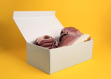 Pair of stylish kid's sneakers in box on yellow background