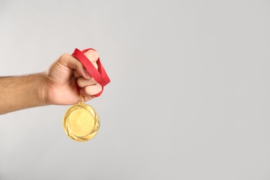 Photo of Man holding golden medal on grey background, closeup. Space for design