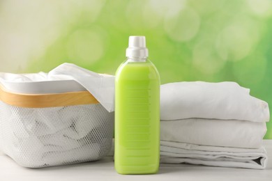 Bottle of laundry detergent and clean clothes on white wooden table