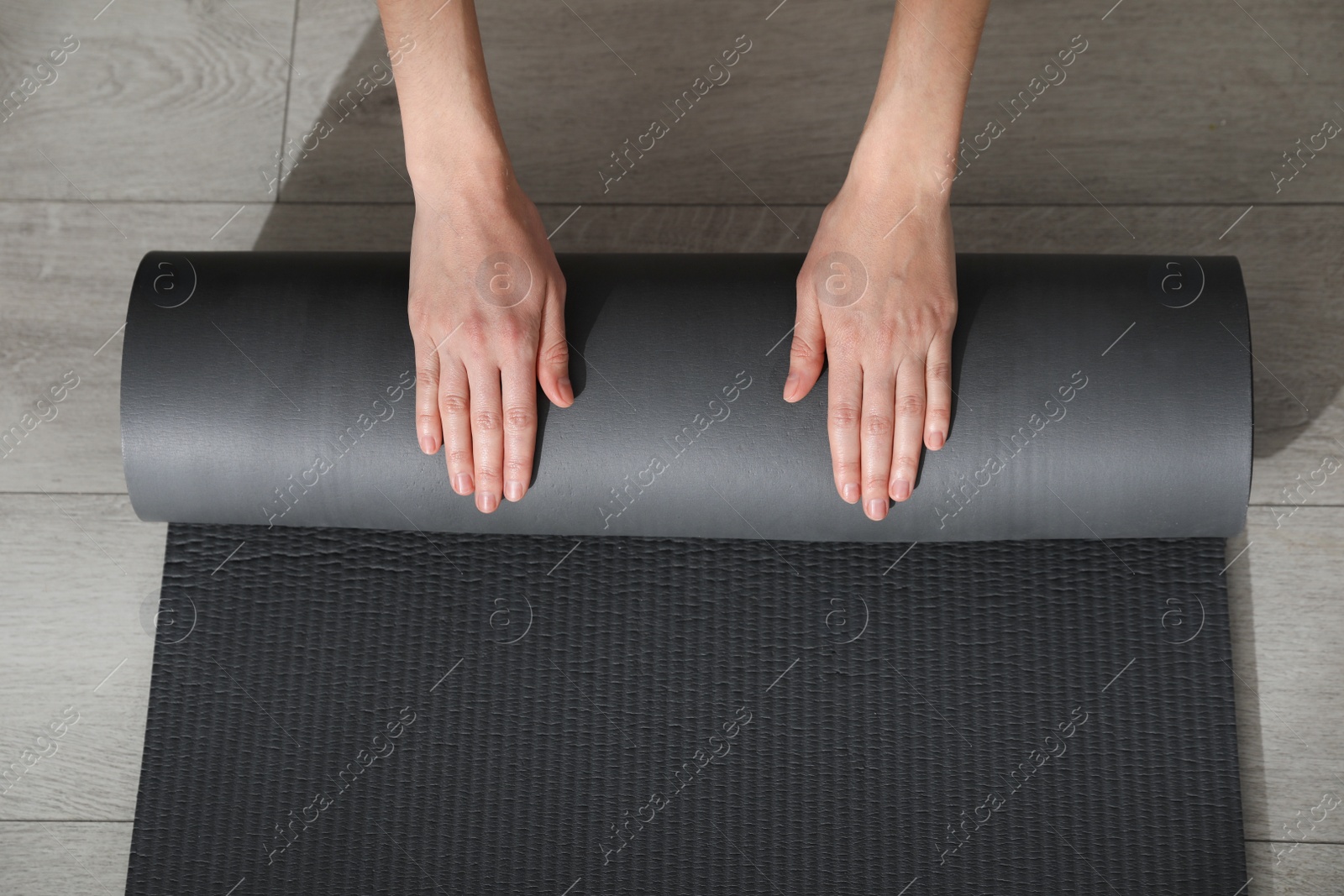 Photo of Top view of woman rolling yoga mat on floor